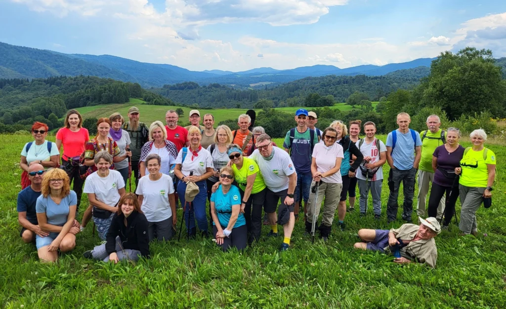 Liczna grupa uczestników wycieczki pieszej PTTK na łące z panoramą Bieszczadów w tle – turystyka aktywna Sanok